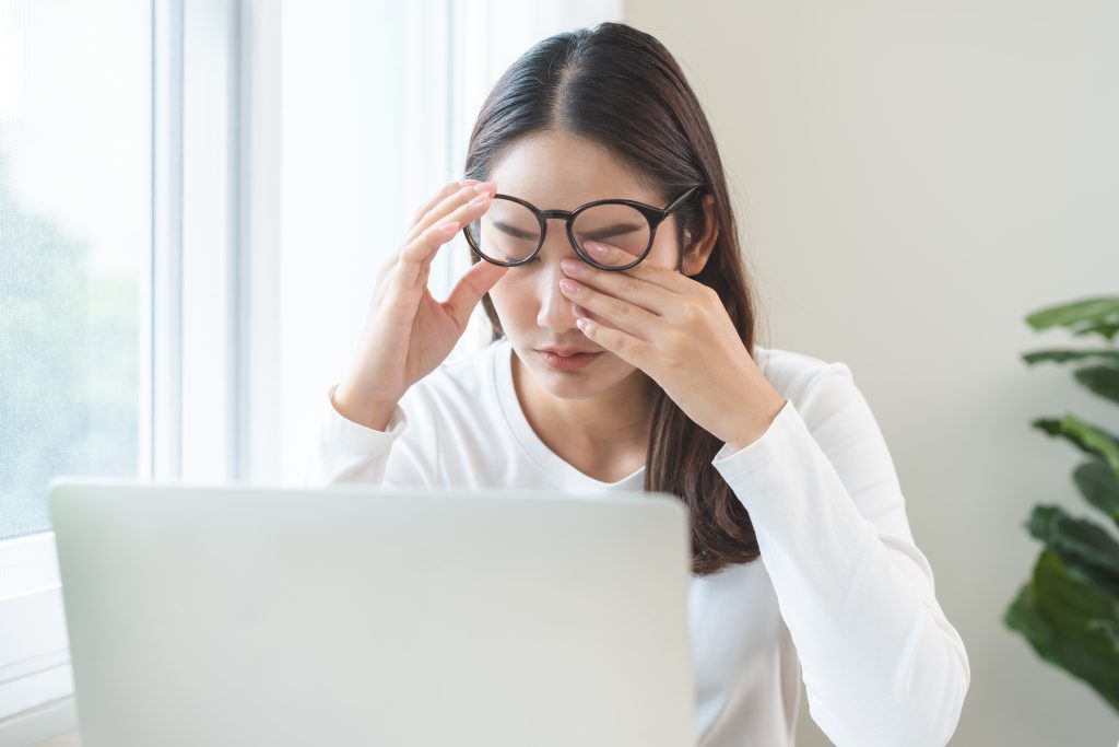 Person sitting in front laptop rubbing eyes from eye allergy needing Eye Exam in Crown Point.