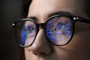Close-up of a person wearing glasses, with computer screen reflections in the lenses—an image highlighting the importance of regular checkups with a St. John eye doctor.