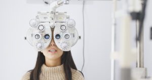 A woman undergoes a Lowell comprehensive eye exam, with a machine carefully positioned over her eyes.